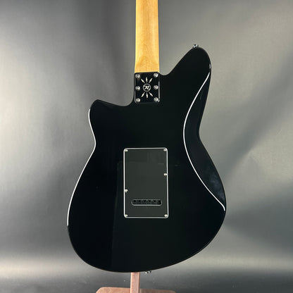 Black electric guitar with a wooden neck on a gray background
