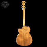 The back of a wooden acoustic guitar, showing a glossy natural wood grain finish, photographed against a solid black background with a Tone Shop watermark in the top-left corner.