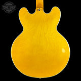 The back of an electric guitar with a glossy yellow-orange sunburst finish, shown against a solid black background with a Tone Shop watermark in the top left corner.