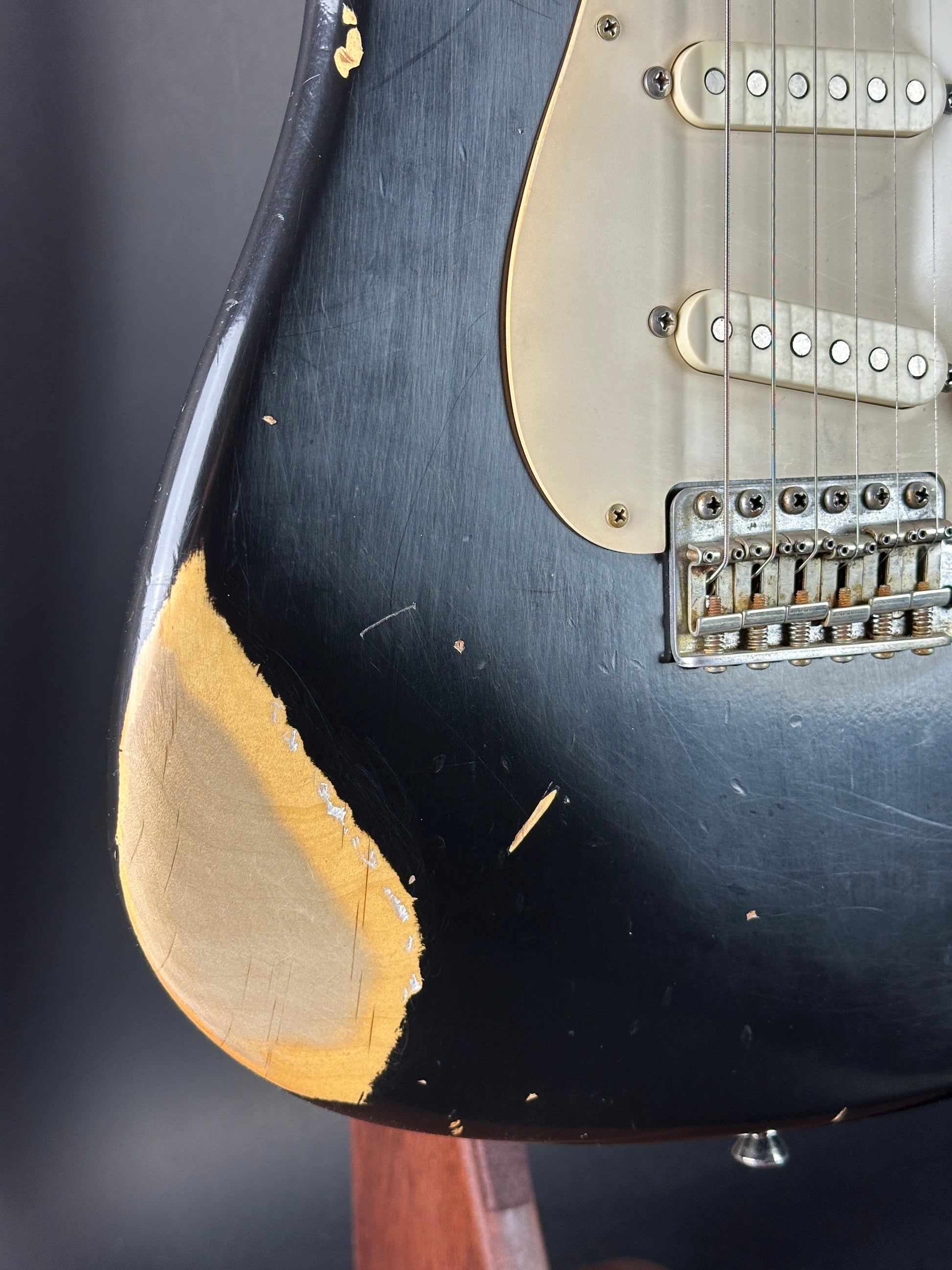 Close-up of a black electric guitar with visible wear on the body.