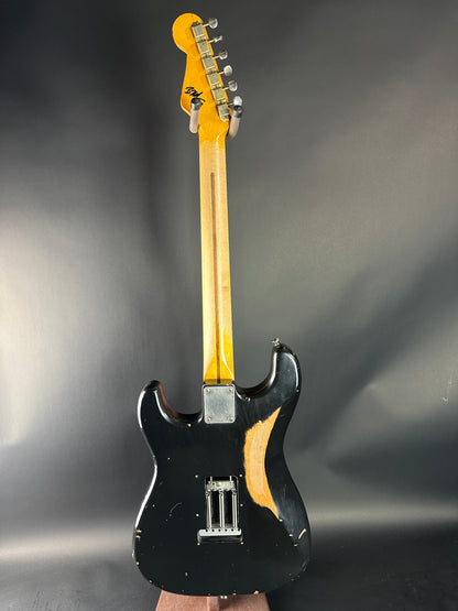 Black electric guitar with a blonde neck on a reflective gray surface