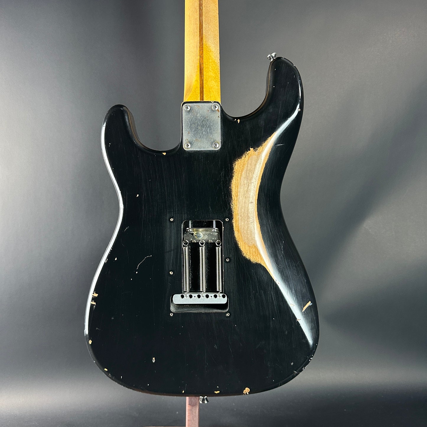 Black electric guitar body with a worn finish on a gray background