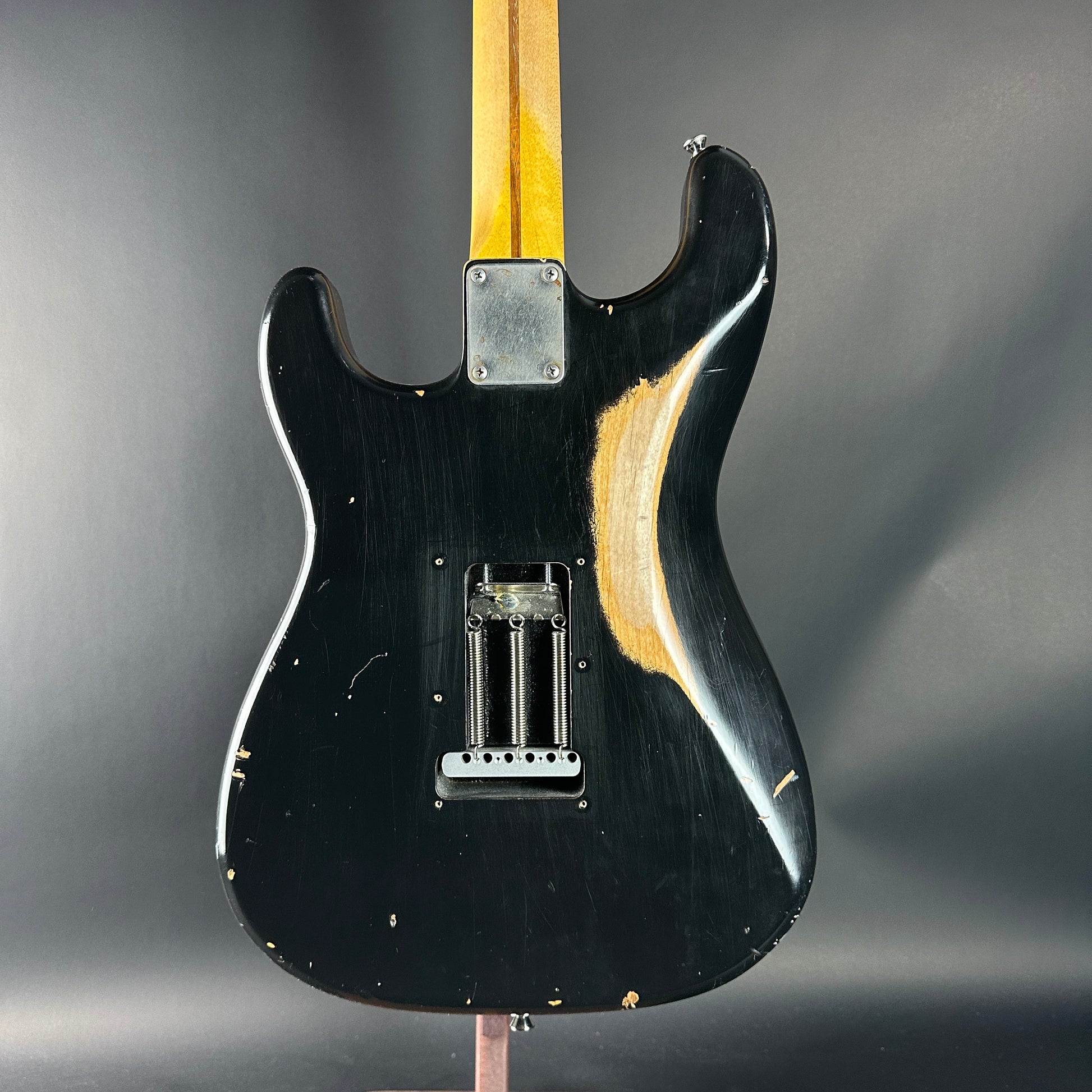 Black electric guitar body with a worn finish on a gray background