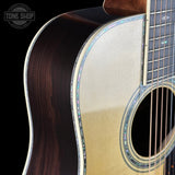 Close-up of an acoustic guitar's body and neck on a black background with 'Tone Shop' logo.