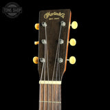 Close-up of the headstock of a Martin & Co acoustic guitar against a solid black background, showing the brand name in gold script, six tuning pegs, and the beginning of the dark wood fretboard.