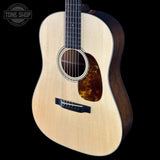 Acoustic guitar with a tortoiseshell pickguard on a black background, featuring the Tone Shop logo.