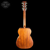 The back view of a wooden acoustic guitar against a solid black background, featuring a warm brown wood finish and a Tone Shop logo watermark in the top left corner.