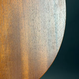 A close-up of a curved wooden surface with warm golden-brown tones and visible wood grain, set against a dark teal background.