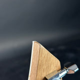 Close-up detail of a guitar headstock corner showing the light wood grain and a silver chrome tuning peg against a dark blurred background.