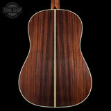 Back view of a wooden acoustic guitar with a visible brand logo in the corner.