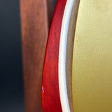 Close-up detail of an electric guitar body showing the red maple wood edge, white binding, and a gold-finish back or inner panel.