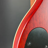 Close-up of a red electric guitar body showing the edge of the wood, a black pickguard, and part of the neck against a dark gray background.