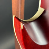 Close-up of a glossy red wooden guitar body with a cream binding edge and a small visible wood grain defect on the lower bout.