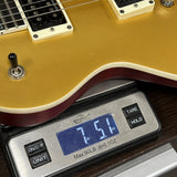 Close-up of a gold electric guitar body resting on a digital scale displaying 7.51 lbs, with part of the guitar including cream pickups and a dark red edge visible.