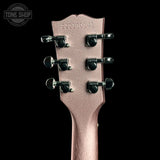 Close-up of the headstock of a guitar in a textured rose gold finish, featuring six black tuning pegs and serial number 2221S0141, set against a solid black background.