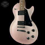 A close-up of an electric guitar body in a metallic rose gold finish with a black pickguard, black humbucker pickups, and chrome hardware, shown against a solid black background. A Tone Shop watermark is visible in the top-left corner.