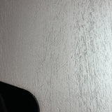 A close-up of a light gray textured surface with fine vertical striations, with a small dark curved shape visible in the bottom-left corner.