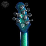 Close-up of a guitar headstock with blue and green glitter finish on a black background, featuring the Tone Shop logo.