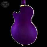 The back of a purple electric guitar with a glossy metallic finish, gold hardware, and a white binding, shown against a solid black background.