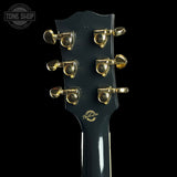 Close-up of the headstock of a black acoustic guitar with gold tuning pegs and a gold 'Hawken' logo, shown against a solid black background.