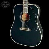 A black acoustic guitar with white binding and a natural wood soundboard, shown against a solid black background. A Tone Shop watermark is visible in the top left corner.