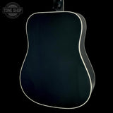 The back of a dark acoustic guitar with a glossy black finish and a contrasting white binding edge, shown against a solid black background.