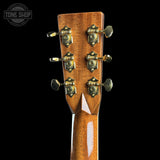 Close-up of the headstock of an acoustic guitar, showing six tuning pegs with decorative sunburst centers and a glossy brown wood finish, set against a solid black background.