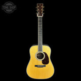 A natural wood acoustic guitar with a dark brown pickguard and headstock, shown against a solid black background. A 'TONE SHOP' watermark is visible in the top-left corner.