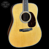A close-up studio shot of a wooden acoustic guitar body against a solid black background, with a Tone Shop watermark in the upper left corner.