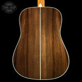 The back of an acoustic guitar showing a rich brown wood grain finish with a white binding edge, set against a solid black background with a Tone Shop logo in the top left corner.