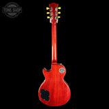 A red electric guitar shown from the back against a solid black background, featuring a glossy cherry red finish, a black pickguard, and a circular gold-toned badge on the backplate.