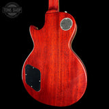 The back of a red electric guitar with a glossy cherry red finish, featuring a silver circular 'Gibson' logo badge and a black pickguard, shown against a solid black background.