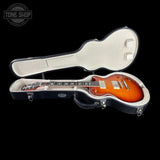 An electric guitar in a black hard case, shown open against a black background. The guitar has a sunburst orange body with a maple neck and chrome hardware.