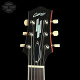 Close-up of a guitar headstock with six tuning pegs, a dark wood finish, and a geometric inlay, photographed against a black background. A Tone Shop watermark is visible in the top-left corner.