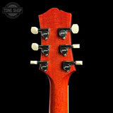 Close-up of a guitar headstock with six black and white tuning pegs, featuring a textured orange-red finish against a solid black background. A Tone Shop watermark is visible in the top left corner.