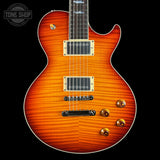 A classic electric guitar with a vibrant sunburst finish, featuring a flamed maple top, gold hardware, and a dark fretboard, shown against a solid black background with a Tone Shop watermark in the top left corner.