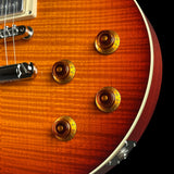 Close-up of an electric guitar body showing a sunburst orange wood finish, four gold-toned control knobs, a chrome bridge, and part of the white pickup cover against a black background.