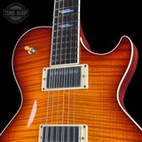 Close-up of an electric guitar body showing a sunburst flame maple wood finish, dual humbucker pickups, and a black fretboard against a black background.