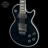 A black electric guitar with white binding and chrome hardware, shown from a side angle against a black background. A Tone Shop watermark is visible in the top-left corner.