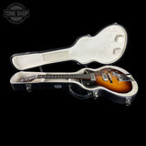 A sunburst electric guitar displayed inside an open black hard case with cream lining, set against a solid black background. A Tone Shop watermark is visible in the top-left corner.