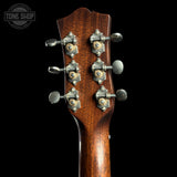 Close-up of the headstock of an acoustic guitar with six silver tuning pegs and a rich brown wood grain finish, set against a solid black background with a Tone Shop watermark in the top left corner.