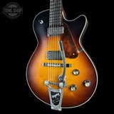 A close-up of a double-cutaway electric guitar against a solid black background. The guitar features a classic sunburst finish transitioning from black at the edges to a warm amber-orange in the center, with a glossy wood grain pattern on the lower bout.