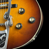Close-up of an electric guitar body showing the sunburst finish, control knobs, and a silver tailpiece against a black background.