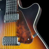 Close-up of a double-cutaway electric guitar showing the sunburst finish, woodgrain pickguard, dual humbucker pickups, and white binding against a black background.