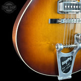 Close-up of a sunburst electric guitar body showing the bridge, pickups, and strings against a black background, with a Tone Shop watermark in the top left.
