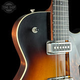 Close-up of an electric guitar body showing a dark black-to-brown sunburst finish, cream binding, a chrome toggle switch, and part of the fretboard against a black background.