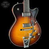 A close-up of a Gibson electric guitar body with a classic sunburst finish, featuring a black pickguard, chrome hardware, and a silver Pedley tailpiece, set against a solid black background.