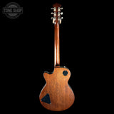 A back view of a wooden six-string electric guitar with a warm brown finish, shown against a solid black background. A Tone Shop watermark is visible in the top-left corner.