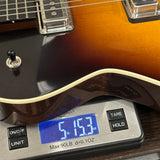 A close-up of a guitar resting on a digital scale displaying its weight of 5.153 oz.