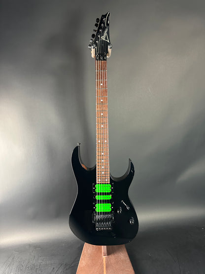 Black electric guitar with green pickups on a gray background